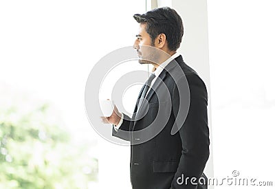 Side view of serious pensive manager having a cup of coffee while looking out at the view through large windows at office Stock Photo