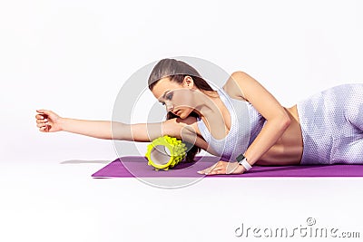 Side view slim sportive woman in white top and tights massaging hands and relieving tension using fitness roller lying on yoga mat Stock Photo