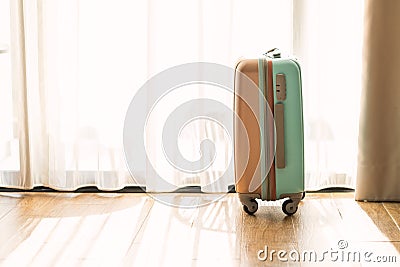 Side view small modern luggage with two tone color, stand on the wooden floor in a hotel room, background of white curtain, space Stock Photo