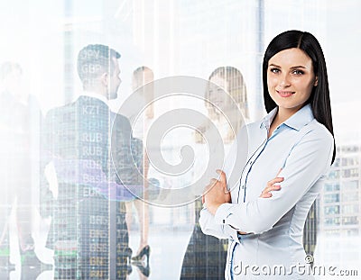 Side view of the smiling brunette woman with crossed hands. A figures of the young professionals in formal clothes on the backgrou Stock Photo