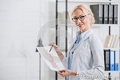 side view of smiling chiropractor in eyeglasses and white coat pointing at human Stock Photo