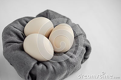 Side view of three unpainted beige eggs in the nest of the grey fabric on a white background. Stock Photo