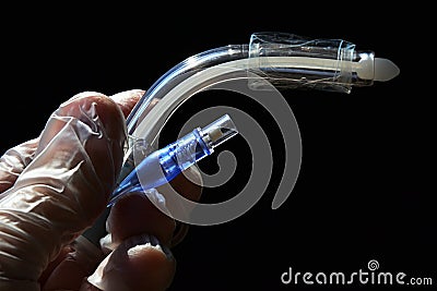 Side view of tracheostomy cannula with deflated cuff and white obturator visible, black background. Stock Photo