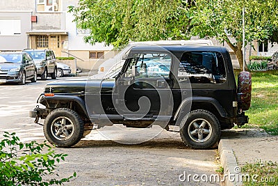 Side view of two door black jeep wrangler parked on an outdoor parking lot near multi-storey apartment building on a sunny summer Editorial Stock Photo