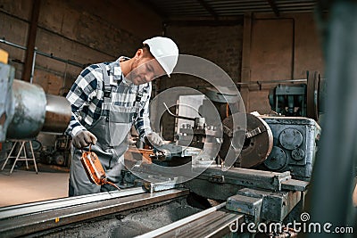 Side view. Using machine. Factory male worker in uniform is indoors Stock Photo