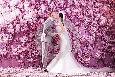 Side view of wedding couple kissing white standing against wall covered with pink flowers Stock Photo