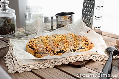 Side view of whole grated pie on a sheet of parchment paper surrounded by kitchen utensils on a wooden table Stock Photo