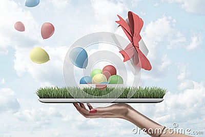 Side view of woman`s hand holding tray owith patch of green lawn with open gift box on top from which colorful balloons Stock Photo