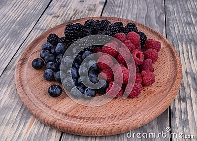 Side view on wooden plate with sumer red, blue and blackberries textured wooden background Stock Photo