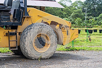 Side view of a yellow road roller that's on the stand by mode without the roll at a park Stock Photo