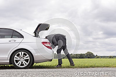 Side view of young businessman looking in trunk of car at countryside Stock Photo