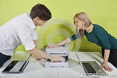 Side view of young businesspeople setting up printer with laptops at desk Stock Photo