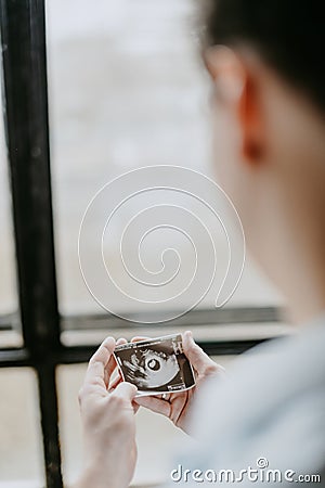 Side view of a young father holding a picture of a baby`s ultrasound in his hands and looking at it with love Stock Photo