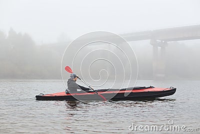 Side view of young kayaker in river, padding, man enjoying water sport in foggy morning with bridge on background, male rowing Stock Photo