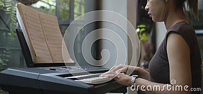 Side view of young woman focusing on sheet music playing electric piano at home Stock Photo