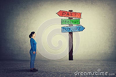 Side view of young woman standing in front of a signpost with arrows shows past, present and future. Lost in time colorful road Stock Photo