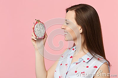 Side view of young woman in summer clothes holding half of fresh ripe pitahaya, dragon fruit isolated on pink pastel Stock Photo