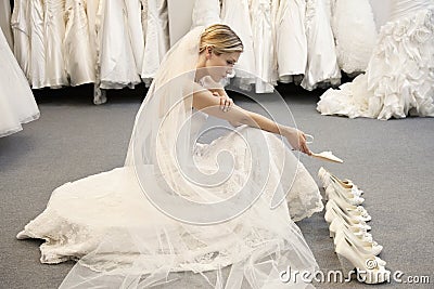 Side view of young woman in wedding dress confused while selecting footwear Stock Photo