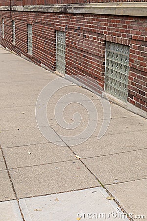 Sidewalk running directly against a red brick building with glass block basement windows Stock Photo