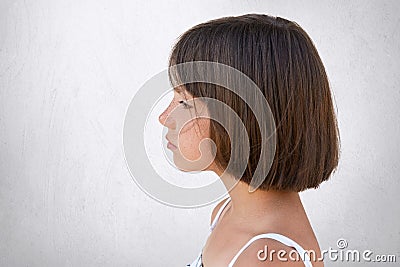 Sideways portrait of adorable freckled girl looking into distance while having dreamy expression over white concrete wall Stock Photo