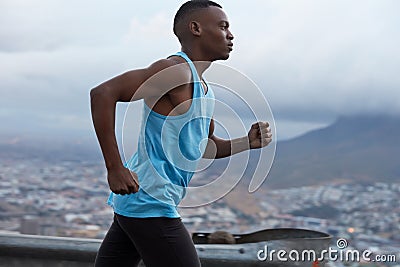 Sideways shot of sporty dark skinned runner wears blue vest, participates in triathlon race, has fitness lifestyle Stock Photo