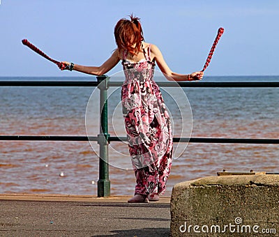 SIDMOUTH, DEVON, ENGLAND - AUGUST 5TH 2012: A young woman entertains passers by with twirling clubs by the iron railings of the Editorial Stock Photo