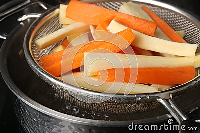 Sieve with cut parsnips and carrots over pot of boiling water, closeup Stock Photo