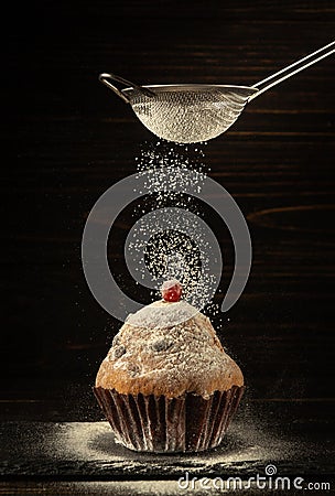 From the sieve, powdered sugar is sprinkled onto a baked red berry muffin. Delicious dessert concept on black background Stock Photo