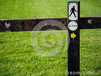 Sign on a fence walking man and direction arrow to the right. and 2 km distance. Stock Photo