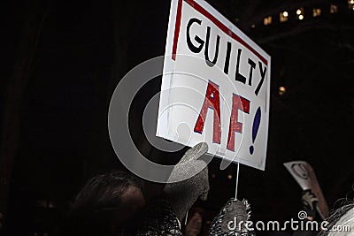 Sign Guilty AF at night-time pre-impeachment rally with gloved finger pointing to message Stock Photo