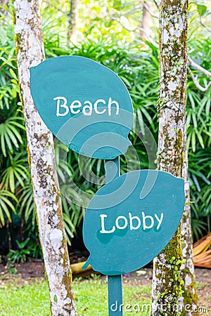 Sign sign hotel lobby and beach, made of wood, in the shape of a leaf, green, road to the beach, on a background of green trees Stock Photo