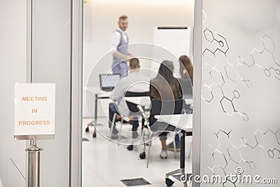 Sign `Meeting in progress`, standing in front of office, while presentation group of people indoors Stock Photo