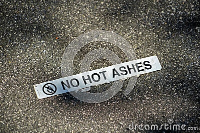 Sign that says no hot ashes on floor of barbeque location with white and black paint in late afternoon shadow Stock Photo