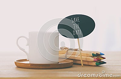 sign with text: SAVE THE DATE next to cup of coffee over wooden table. Stock Photo