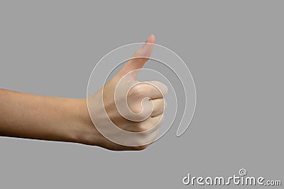 The sign of the thumb. Hand with white skin, showing the like sign, on a gray isolated background. Close-up, selective focus Stock Photo