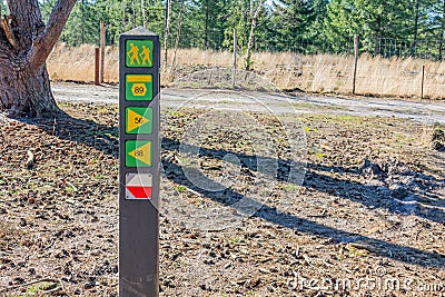 Signpost of different hiking trails in yellow, one with white and red, a path and green leafy trees Stock Photo