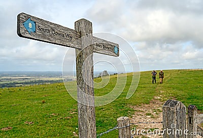 A signpost shows the route of the South Downs Way with two unrecognizable hikers Editorial Stock Photo