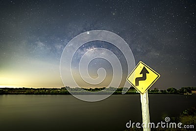 Signs, signs, beware of curves at night, behind the sign with the Milky Way. Stock Photo