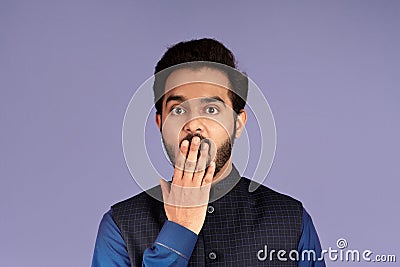 Silence or mistake concept. Shocked Indian man covering mouth with his hand over lilac background Stock Photo