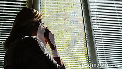 Silhouet van een jonge vrouw door het venster Hij bekijkt de straat door de zonneblinden, drinkt koffie van een kop kijkt stock video Silhouet van een jonge vrouw door het venster Hij bekijkt de straat door de zonneblinden, drinkt koffie van een kop kijkt stock video