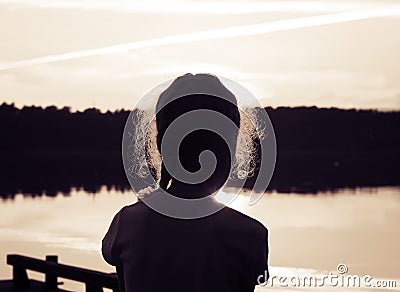 Silhouette of adorable little girl on the lake at sunset. Toned Stock Photo