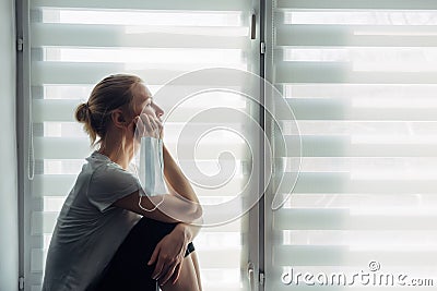 Silhouette of alone woman sitting on the windowsill on the background of window. Quarantine, self-isolation, stay at home. Concept Stock Photo