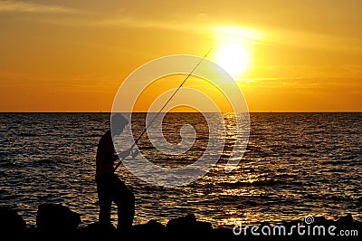 Silhouette of angler fishing on the rock at the beach of malacca Stock Photo