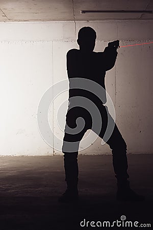 Silhouette of an armed man holding his gun and pointing with his laser beam Stock Photo