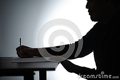 Silhouette asian man writing on table. Beared man writing on Notebook. Freelancer man Blogger writing at Home on desk Stock Photo