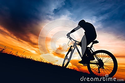 Silhouette of athlete riding mountain bike on hills at sunset Stock Photo