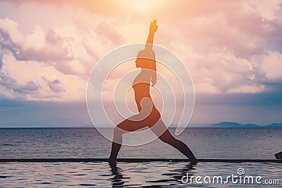 silhouette Athletic woman practice yoga Warrior one pose to meditation summer vacation on pier with sunset sea beach Stock Photo