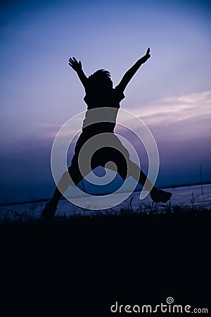 Silhouette back view of child enjoying and jumping at riverside. Stock Photo