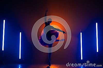 Silhouette of ballerina is practicing elements in studio with neon colorful light. Young woman dancing in classic tutu Stock Photo