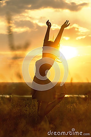 Silhouette of a beautiful girl dancind and spinning in a dress at sunset in a field, happy young woman enjoying nature Stock Photo
